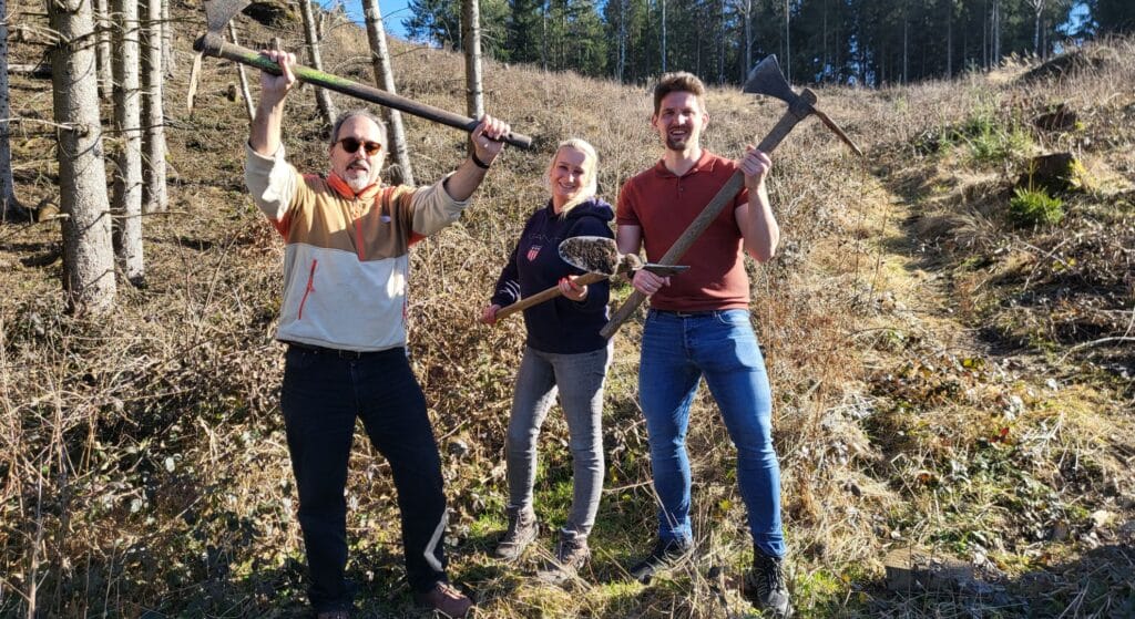 up to data Tree-Planting | Three team members holding gardening tools outdoors in forest setting during environmental conservation or team building activity